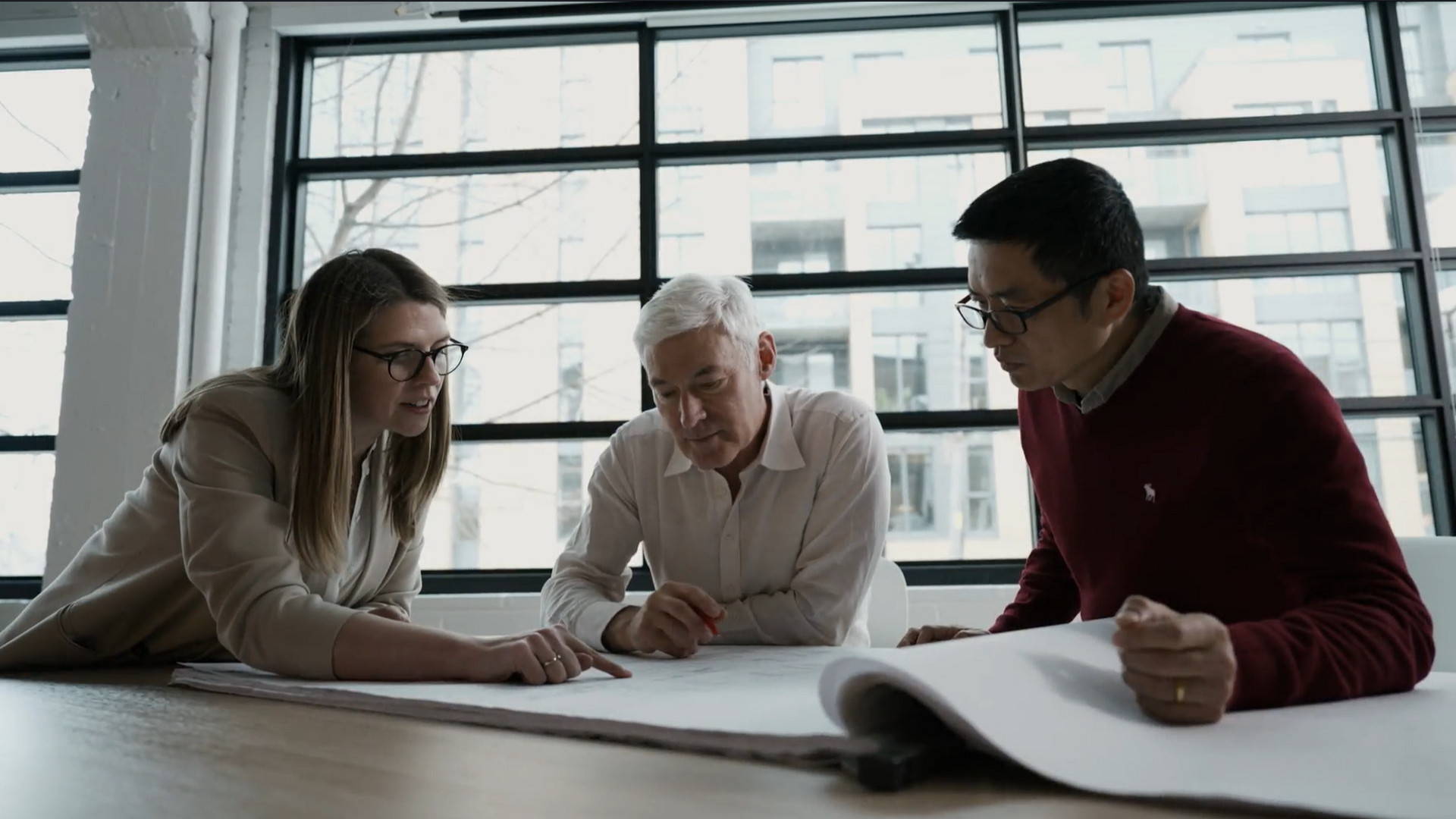 Three members of the team are analyzing an architectural plan at the GKC headquarters, Architecture and Design.